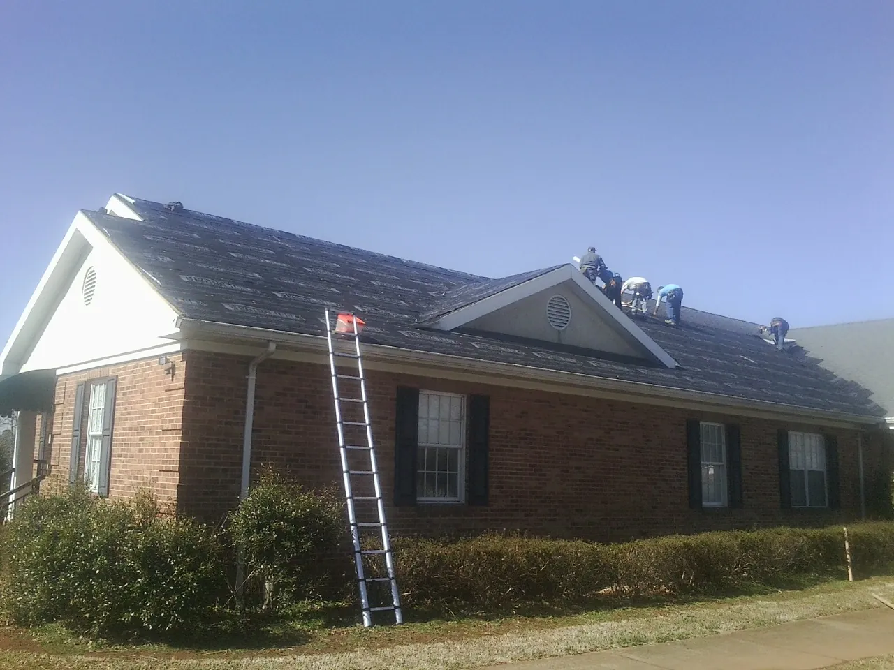 Crew tearing shingles off a brick ranch roof with a ladder set — Metal Roof Repair work by our crew in Waterloo